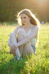 Fototapeta na wymiar Hübsche junge Frau trägt Hot Pants und Oberteil bauchfrei sitzt im Gras an einem sonnigen Sommertag im Park