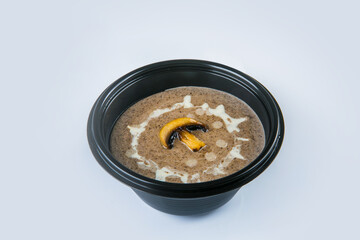 Mushroom cream soup with champignons and sour cream sauce served in plastic delivery bowl. Dish isolated on gray background. Vegetarian first dish in black plate. Vegan Food isolation
