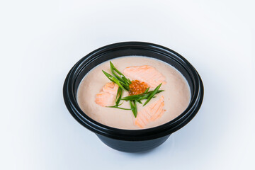 Salmon cream soup with salmon fillet pieces, red caviar and spring onion scallions served in plastic delivery bowl. Dish isolated on gray background. Asian first dish in black plate. Food isolation