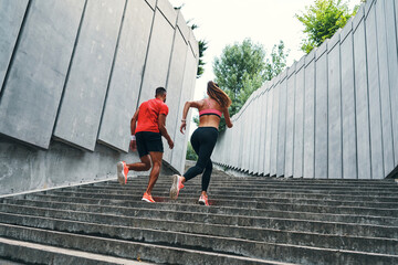 Full length of two athletes in sports clothing running up the stairs while practicing outdoors