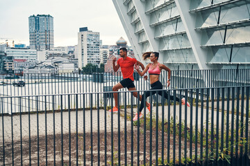 Full length of young beautiful woman and man in sports clothing enjoying morning jogging while practicing outdoors