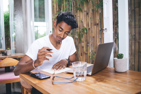 Ethnic young man taking notes on paper in cafe
