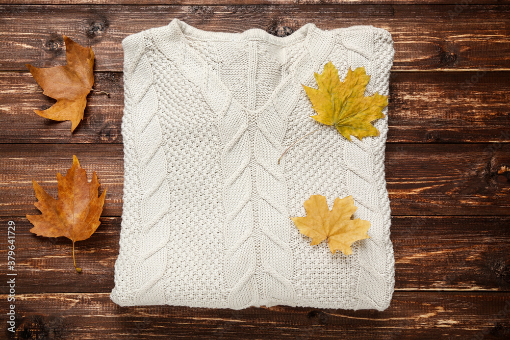 Poster Woolen sweater with autumn leafs on brown wooden table