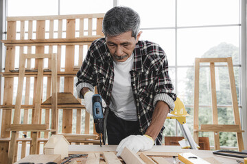 A senior carpenter using electric drill of house wooden interior accessories for further refinement within a building or condominium. Construction concept.