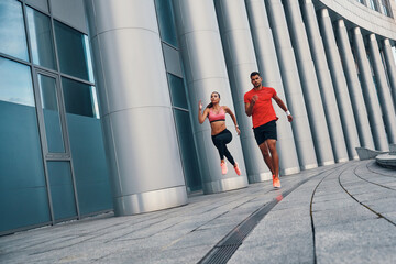 Full length of young beautiful woman and man in sports clothing enjoying morning jogging while practicing outdoors on the city street