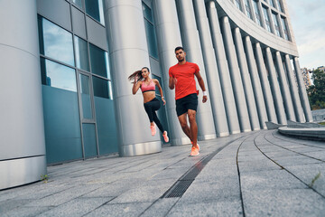 Full length of confident fit couple in sports clothing enjoying morning jogging while practicing outdoors on the city street