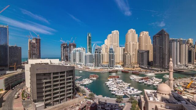 Yachts in Dubai Marina flanked by the Al Rahim Mosque and residential towers and skyscrapers aerial timelapse during all day with shadows moving fast. Modern high rise skyline with boats and wooden