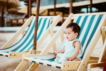 9 Months  asian baby sitting on beach chair with sea beach as background, summer concept