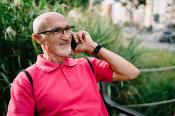 Adult male pensioner in optical spectacles for provide eyes correction enjoying international smartphone conversation during free time, carefree man in glasses calling via modern mobile gadget
