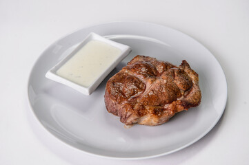 Single grilled Pork meat steak on gray plate, served with white sauce. Close up of tasty main dish without garnish

