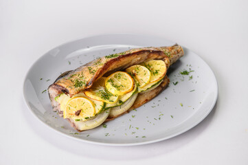 Close up of baked mackerel with lemon slices and onion on gray plate isolated on gray background. Grilled fish served with fresh herb dill. Food isolation 
