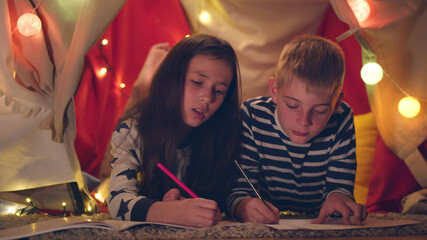 Happy preteen boy and girl drawing together while lying in play tent