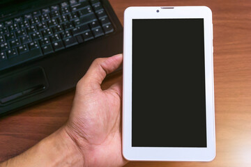 Mockup image for top view of a hand of a man holding a tablet with a blank screen and laptop on table