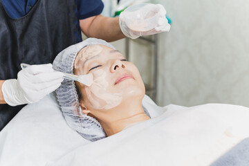 Woman having facial treatment at spa with beautician applying mask on lady face.