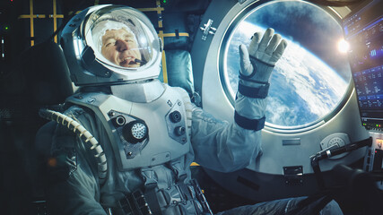 Portrait of a Happy Astronaut on a Space Ship In Orbit. Cosmonaut in a Futuristic Space Suit is Full of Joy and is Waving Hand on a Video Call. VFX Graphics Shot from the International Space Station.