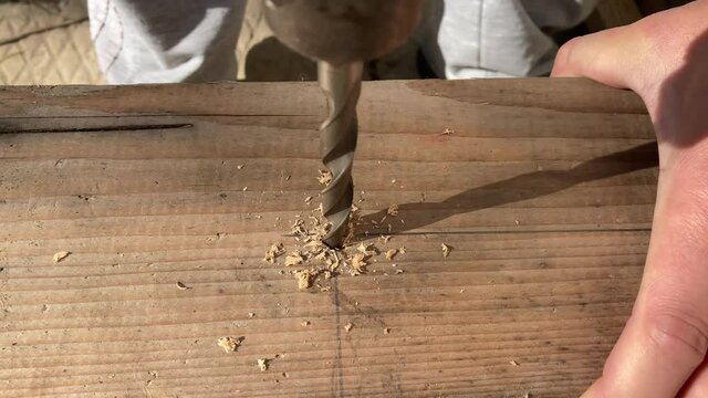 Drilling a hole in wood. The worker performs locksmith work with a drill. Wood shavings from metal cutting tools