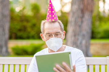 Alone senior man wearing party's cap and protective mask celebrates his  birthday with his family on video call during the coronavirus epidemic