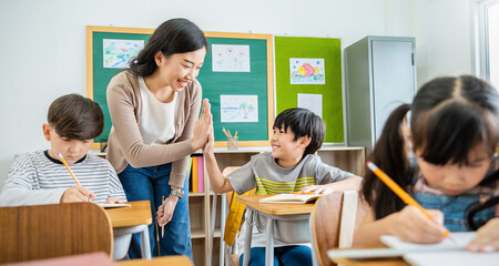 Pupil boy hi five with teacher in classroom at elementary school. Student boy studying in primary school. Children writing notes in classroom. Education knowledge, successful teamwork concept