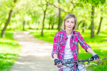 Fototapeta na wymiar Portrait of a sporty senior woman on a bicycle at summer park. Empty space for text