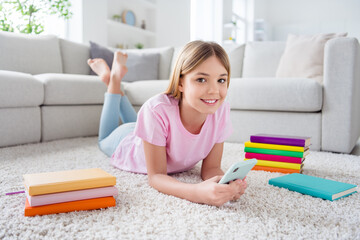 Full body photo of positive kid girl lying floor carpet use cellphone enjoy social media communication conversation repost subscribe in house indoors