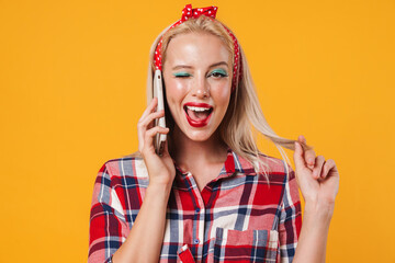 Image of joyful blonde pinup girl winking while talking on mobile phone