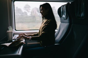 Cheerful Asian woman messaging on laptop in bus