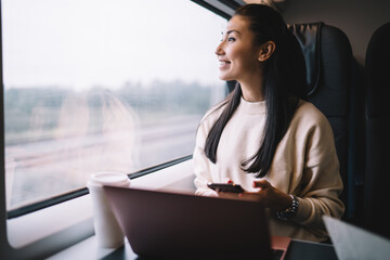 Satisfied ethnic woman using smartphone and looking outside in bus