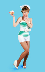 Pinup style girl dressed as pastry chef on blue background. He carries a small cake in his hand.