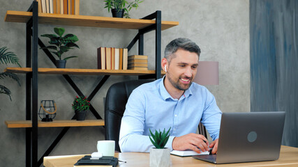 Smiling gray-haired bearded man teacher tutor at home office wear wireless earphones teaches students remote online video conference call chat web cam laptop computer