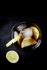 Glass of cola with lemon and ice cubes. Dark stone background. Top view. Close up.	