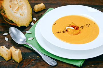 Creamy pumpkin vegetable soup puree with fresh vegetable, seeds and smoked ham in white plate