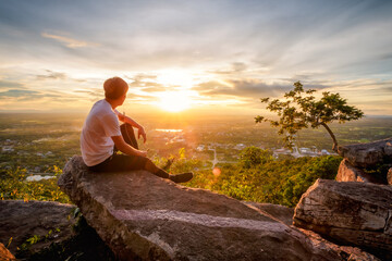 man sitting relax on top of a moutain watching the sunset