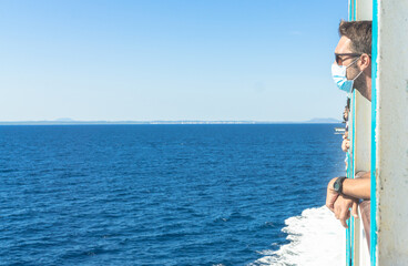 Man wearing face mask traveling by ferry at summer holidays during coronavirus pandemic. New normal Concept