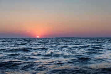 Sunset in the ocean with large sun dusk soft waves and red cloudy sky. Sea sunrise background. Landscape photography