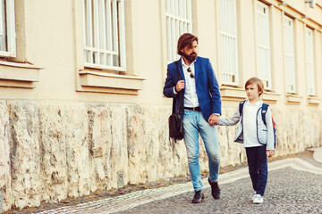 Fashionable father and son walking at street. Parent with kid going home after school.