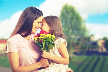 Mother and daughter with bouquet of flowers on blurred background.