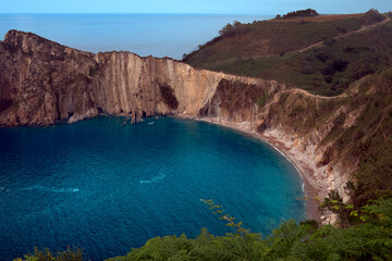 Top view of a lonely cove with crystalline water surrounded by cliffs. Sea horizon and blue sky in the background