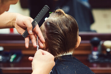 Cute little boy getting haircut by hairdresser at the barbershop. Barber man doing kid the...