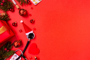 Christmas banner with a Phonendoscope wearing a Santa Claus hat. Nearby lie red balls, a heart, a gift box, branches of a Christmas tree, pills, and medical test tubes. Medical banner concept 