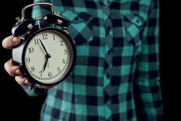 Woman in green shirt holding vintage alarm clock. Black alarm clock in a woman's hand on the black...