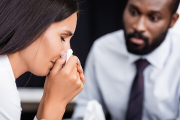 selective focus of crying woman wiping face with paper napkin near serious african american psychologist - obrazy, fototapety, plakaty