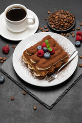 portion of Classic tiramisu dessert with raspberries and blueberries and cup of coffee dark concrete background
