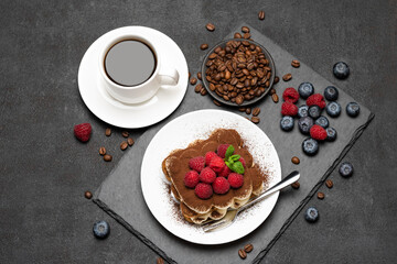 portion of Classic tiramisu dessert with raspberries and blueberries and cup of coffee dark concrete background
