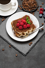 portion of Classic tiramisu dessert with raspberries and blueberries and cup of coffee dark concrete background