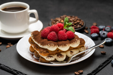 portion of Classic tiramisu dessert with raspberries and blueberries and cup of coffee dark concrete background