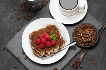 portion of Classic tiramisu dessert with raspberries, cup of espresso and coffee maker on dark concrete background
