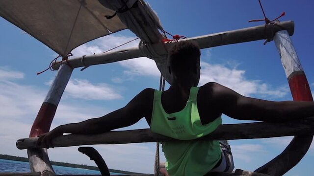 Back of a Young Black African man on a wooden Sail Dhow boat Sit on the Nose and Looking Forward in Green t-shirt Hakuna Matata