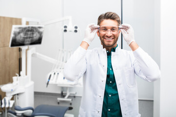 Portrait of a smiling handsome male dentist wearing protective glasses at a modern dental clinic. Modern dentistry
