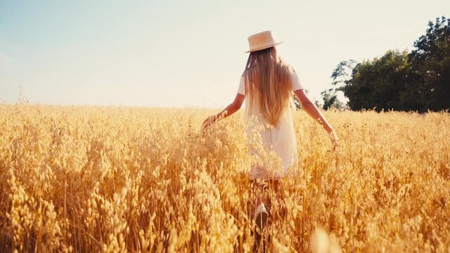 back view of girl in white dress and straw hat walking in wheat field