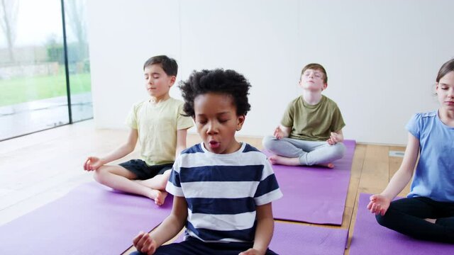 Group of children sitting on exercise mats and meditating in yoga studio - shot in slow motion 